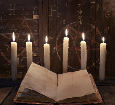 Black magic ritual with burning candles and open book against wooden background.