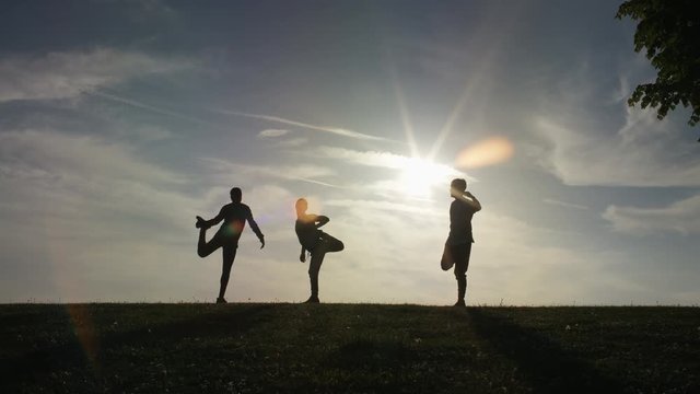 Silhouette of 3 people warming up before a workout session at sunset