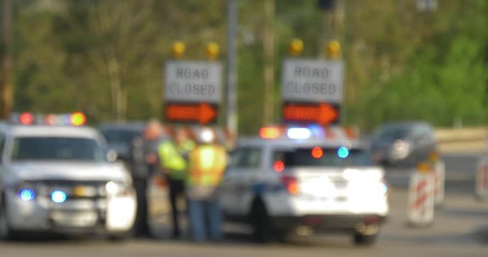 Defocused shot of a closed road with a police car blocking the street as cars pass by.	 	