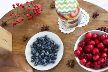 Red cherry, blueberry in the white bowl, water with lemon and strawberry in glass jar on the table. Fruit, fruits. berries. Summer vibes