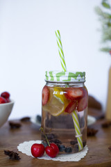 Glass jar with lemonade and green straw. Water with fruit, lemon, strawberry and blueberry. Cherry. Summer vibes
