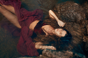 beautiful young woman in red dress lying down in water