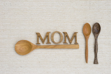Mother's day concept background, natural texture wooden spoon with mom wooden text over canvas texture background, mom's kitchen