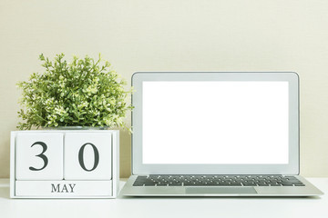 Closeup white wooden calendar with black 30 may word with white blank space at center of computer notebook on white wood desk and cream wallpaper textured background , selective focus at the calendar