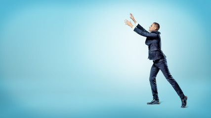 A businessman in side view with both hands raised up trying to catch something above. - Powered by Adobe