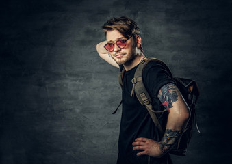 A man with backpack dressed in a black t shirt and red sunglasses.
