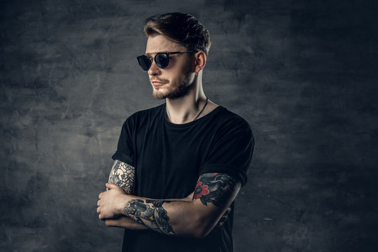 Portrait of positive hipster male with tattoos on his arms over grey vignette background.
