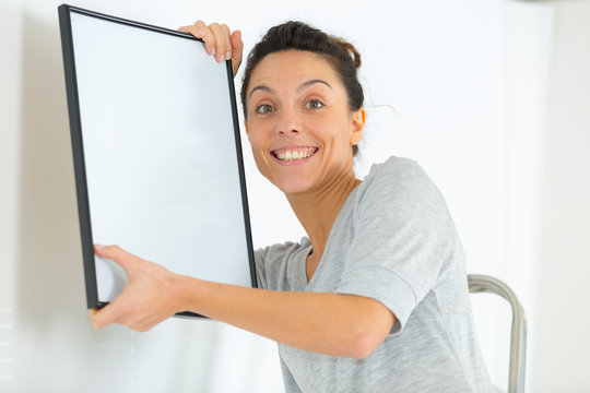 portrait of woman hanging blank picture frame on wall