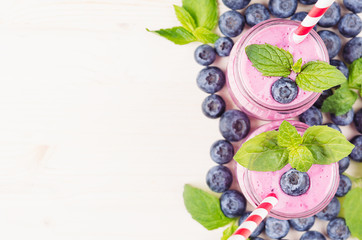 Decorative border of violet blueberry fruit smoothie in glass jars with straw, mint leaves, berries, close up, top view. White wooden board background, copy space.