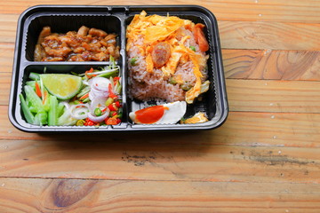 fried rice with shrimp paste include mango, egg, pork, onion, vegetable in box black / Thai style food on a wood table background