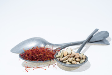 Raw Organic Red Saffron and Cardamom Spices in old tin spoons on white  background