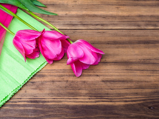 Pink tulips, floral arrangement on wooden background with green paper and space for message. Background for Mother's Day, 8 March and other greeting cards or invitations for lovely women. Soft focus.