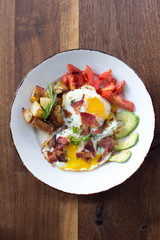 Eggs over medium with a side of avocado, tomato, bacon, and potatoes