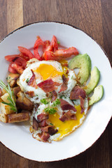 Eggs over medium with a side of avocado, tomato, bacon, and potatoes
