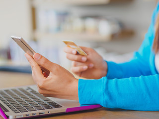Fototapeta premium Pretty Young womans hands holding a credit card and using smartphone and laptop computer for online shopping. Online payment. Female working on smart phone laptop in a cafe.