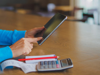 Fototapeta premium Pretty Young womans hands holding and using tablet for online shopping, bill, pencil and calculator on the table. Online payment. Female working on tablet in a cafe.