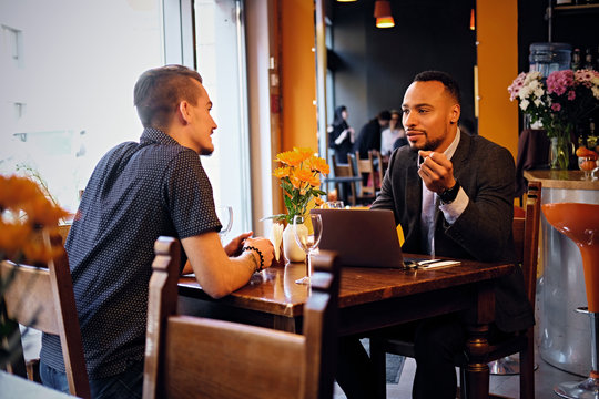 Two men talks and using a laptop in a restaurant.