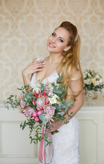 Pretty young Bride.blonde-haired woman with wedding hair-style with a long tail. Boudoir morning of the bride. Looking on her bouquet