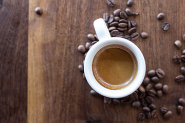 Freshly brewed espresso surrounded by coffee beans on a warm walnut wood table 