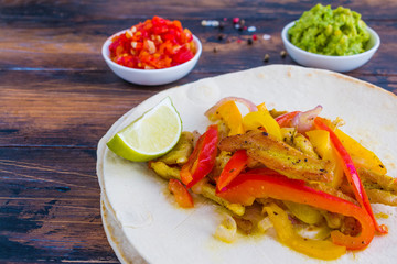 Chicken fajitas, fillet roasted with bell peppers and red onion, tortillas and traditional Mexican sauces salsa and guacamole on the wooden rustic table.