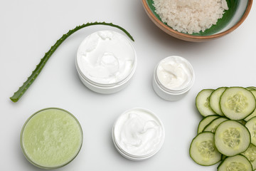 Top view of facial cream in containers, cucumber slices and aloe vera plant isolated on white