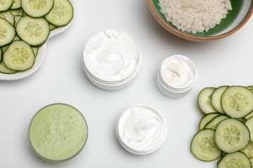 Top view of facial cream in containers and cucumber slices isolated on white