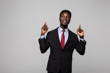 Handsome young African man in suit pointing up and smiling while standing against grey background