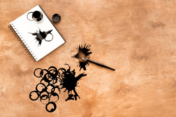 Top view of ink container, fountain pen, notebook and ink splashes on table