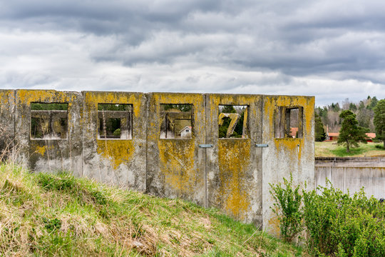 Abandoned concrete ruin on grass hill with square openings against cloudy sky.