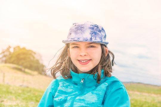 Portrait of cute girl in blue jacket and cap with wind in her hair, outdoors in open landscape.