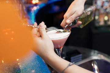 Bartender is adding ingredient in glass at bar counter, at night club