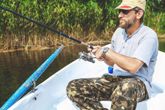 Fisherman with beard sitting in boat and holding fishing rod