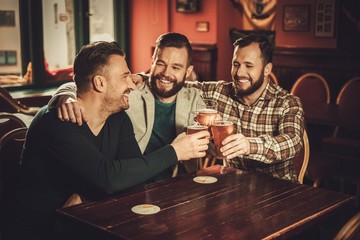 Cheerful old friends having fun and drinking draft beer in pub.