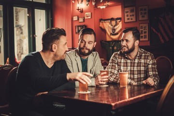 Cheerful old friends having fun and drinking draft beer in pub.