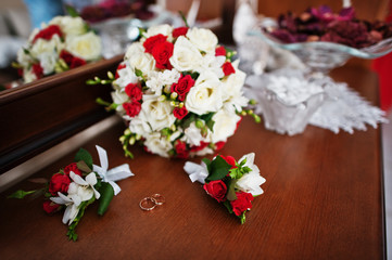 Wedding rings with bouquet and buttonhole on wooden background.