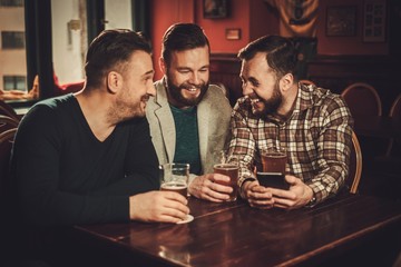 Cheerful old friends having fun and drinking draft beer in pub.