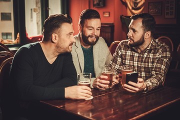 Cheerful old friends having fun and drinking draft beer in pub.