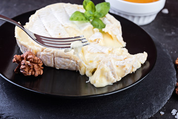 Camembert cheese with walnuts and basil on dark stone board