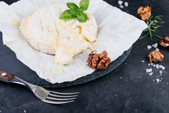 Camembert cheese with walnuts and basil on dark stone board
