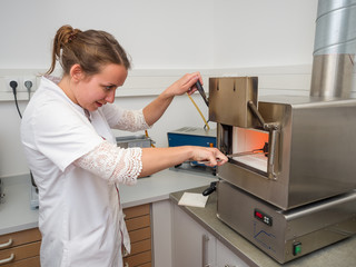 Female Dental Technician putting a Muffles in the Oven using Tongs