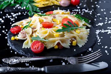 Pasta salad in slate plate with tomatoes cherry, tuna, corn and arugula.  ingredients. Italian food.