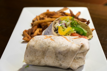 A Greek vegetarian wrap served with golden fries on a white plate.