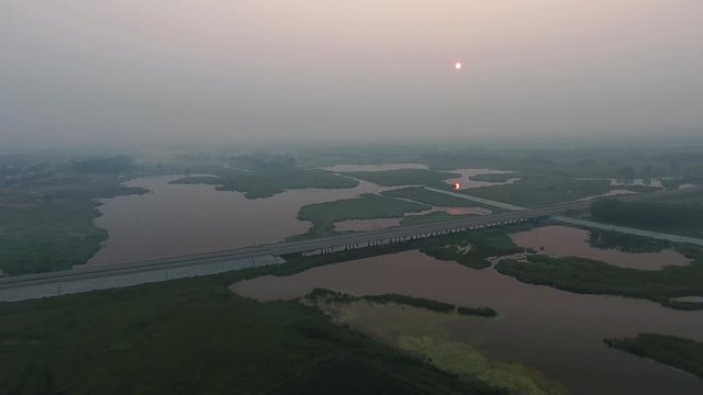 Aerial View. The picturesque landscape with river, highway bridge, trees and field with Incredible sun. Morning Fog.