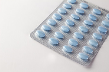 Blue oval pills in blister package on white close up