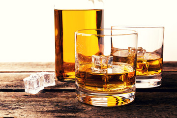 whiskey glasses and bottle on wooden table against white background