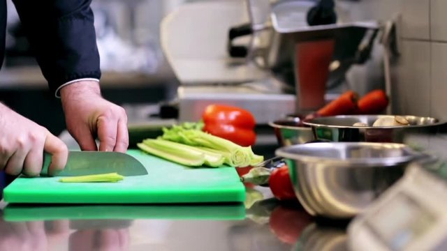 hands of male chef cook chopping celery in kitchen