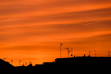 Red sky sunset with clouds, roofs, antennas and plane