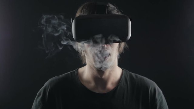 vaper man in vr hemlet exhaling clouds of smoke with e-cigarette vape in slowmotion