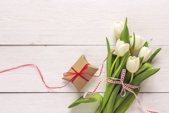 White tulips and gift box with red ribbon on a white painted wooden background and empty space for text.