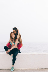 Two young beautiful girlfriends sitting on the background of the sea